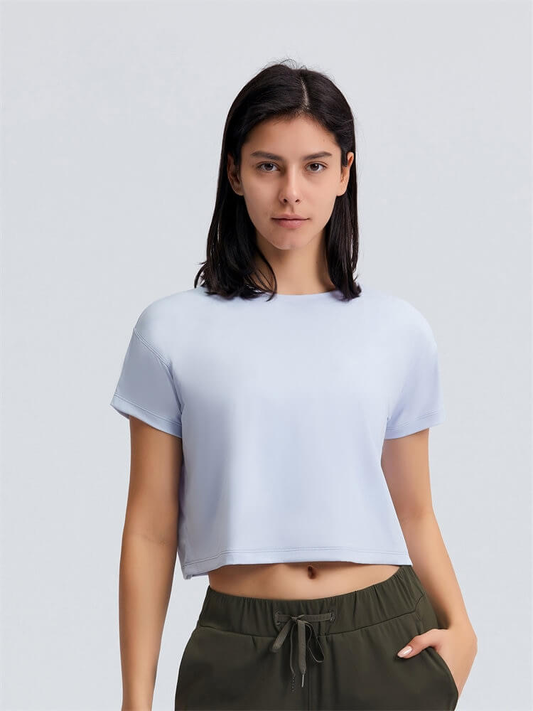 Woman modeling loose fit workout solid crop t-shirt in white, designed for yoga, short sleeves and breathable fabric, perfect flexibility.
